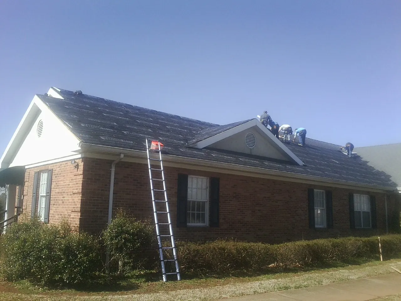 Crew tearing shingles off a brick ranch roof with a ladder set — Emergency Roof Repair work by our crew in Cohutta