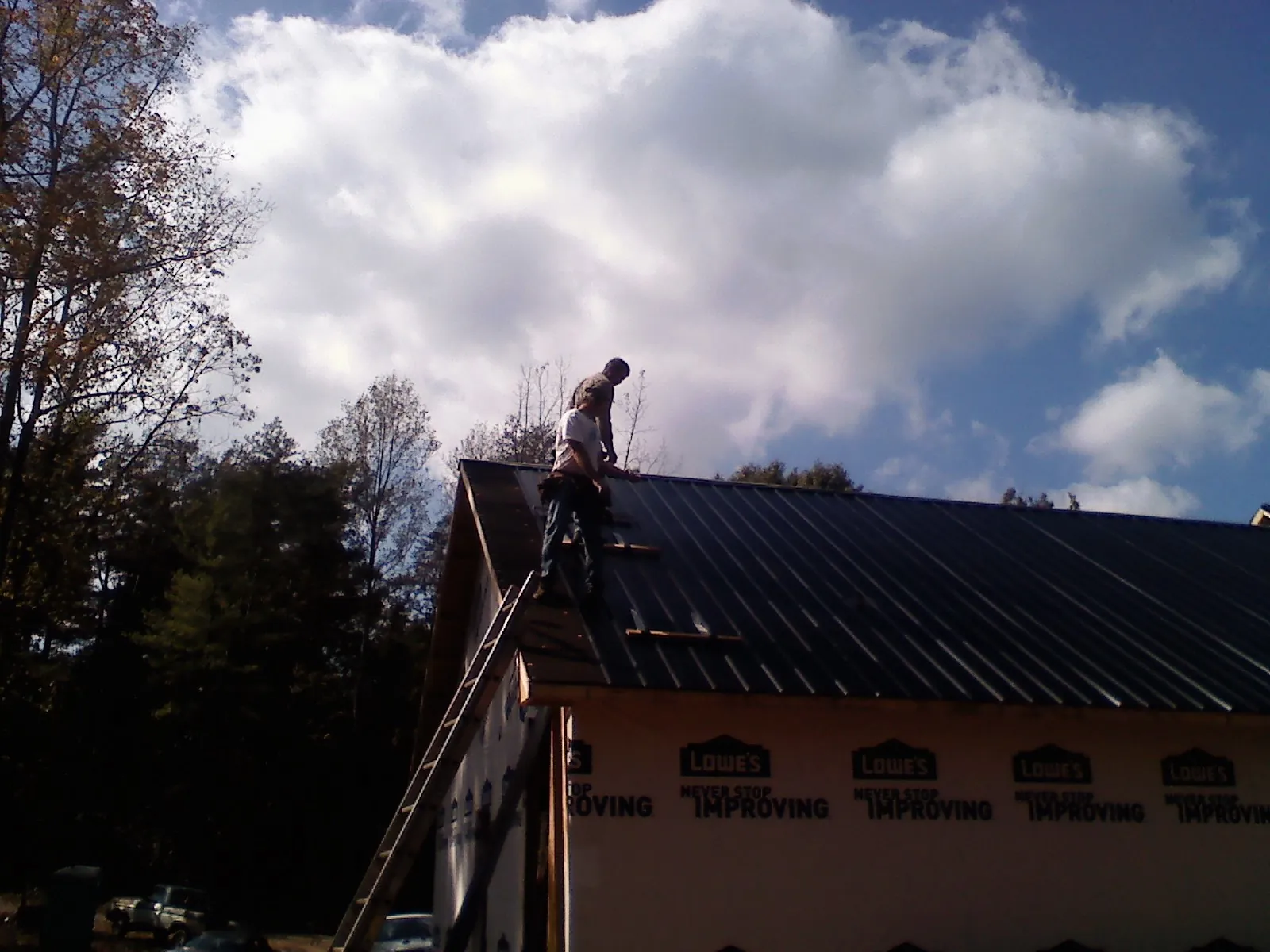 Roofer fastening dark metal panels high against a cloudy sky, from a Roof Inspection job in Cohutta
