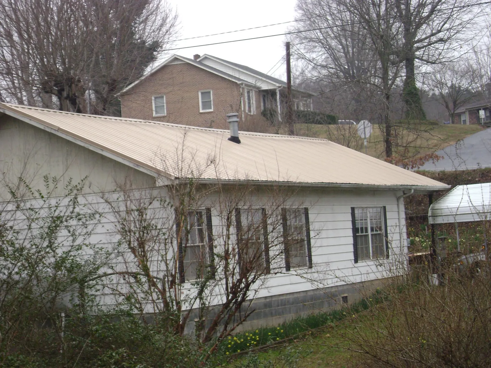 Tan metal roof on a white sided house set into a hillside — Commercial Roofing by Roofing Brothers in Cohutta