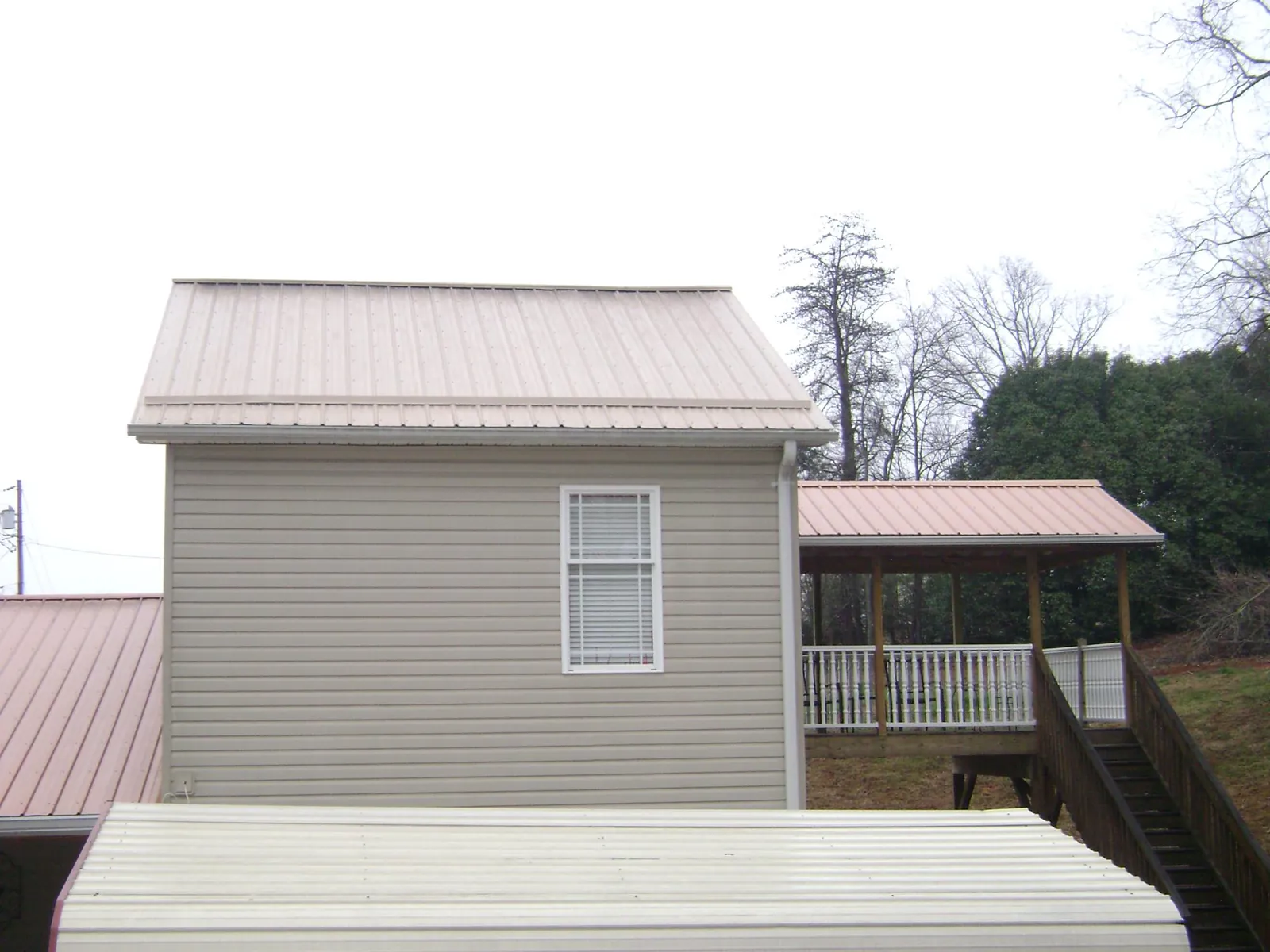 Tan metal roofs on a two story addition and attached porch, from a Roof Replacement job in Cohutta